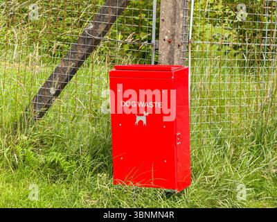 Roter Metallbehälter für Hundeabfälle, der an einem Zaun in einem Publadenpark befestigt ist. Keine Personen. Stockfoto