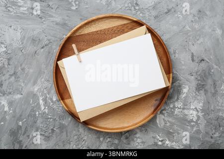 Leere Einladungskarte, Umschlag und Holztablett auf grauem, strukturiertem Tisch, Draufsicht Stockfoto
