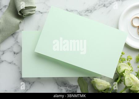 Hochzeitseinladungskarten, goldene Ringe und Blumen auf weißem Marmortisch, flacher Lay Stockfoto
