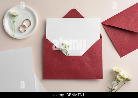 Hochzeitseinladungskarten, Umschläge, goldene Ringe und Blumen auf beigefarbenem Hintergrund, flache Lay Stockfoto