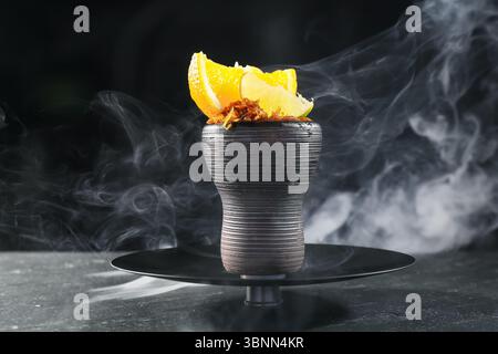 Shisha Schüssel mit Zitrusfrüchten und Rauch auf schwarzem Tisch, Nahaufnahme Stockfoto
