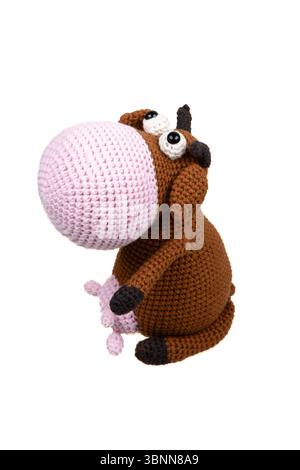 Handgefertigtes Häkelspielzeug eines niedlichen Cartoonstiers mit übergroßer rosa Schnauze und breiten ausdrucksstarken Augen auf weißem Buckelboden. Stockfoto