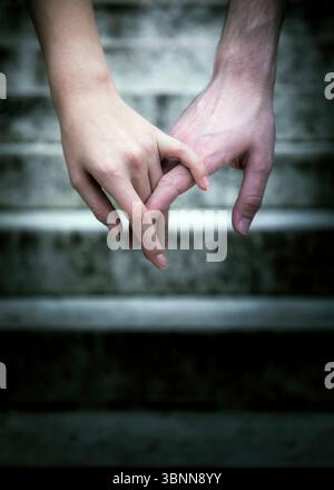 Eine Nahaufnahme von zwei Händen, einer männlichen und einer weiblichen, verflochten. Die Hände sind miteinander verschlossen, die Finger sind verschränkt, was auf eine Verbindung hindeutet Stockfoto