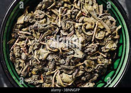 Lose grüne Teeblätter. Getrocknete Kräuterblätter in grüner Schüssel. Natürliche organische Getränkezutat. Gesundes Antioxidans-Getränk Textur. Stockfoto