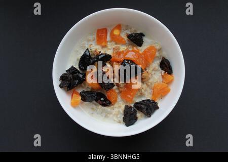 Haferflocken mit Honig und getrockneten Früchten auf schwarzem Hintergrund. Stockfoto