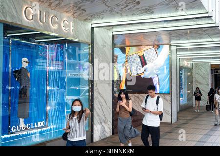 Shopper laufen am italienischen Luxusmodemarke Gucci-Logo vorbei und laden in Hongkong ein. Stockfoto