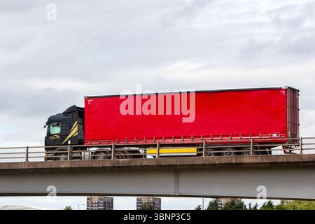 Der schwarze Scania-Gelenkwagen mit einem roten, vorhangseitigen Anhänger von A.K.J Transport überquert eine Fertigbetonbrücke auf der A5 in Tamworth, Großbritannien. Stockfoto