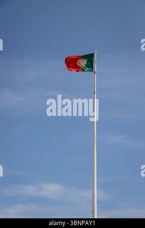 Die portugiesische Flagge winkt auf einem hohen Pfosten vor einem klaren blauen Himmel, die bei Tageslicht im Freien gefangen wurde, um die nationale Identität zu repräsentieren Stockfoto