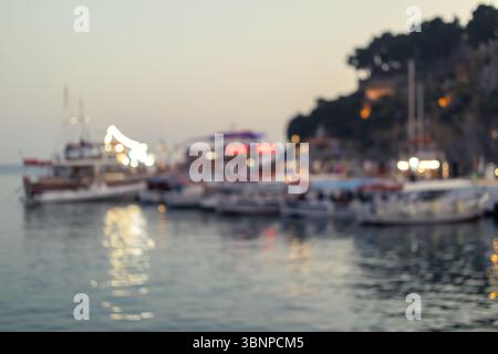 Eine unscharfe Aufnahme eines ruhigen Hafens in der Abenddämmerung, mit einer Ansammlung von Booten, die sanft auf dem Wasser wippen. Das sanfte Leuchten der Boote A Stockfoto