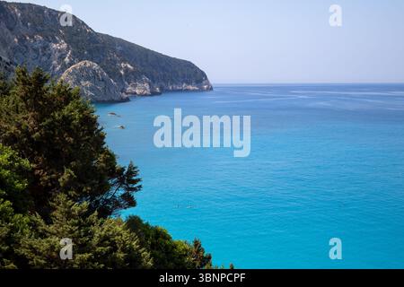 Ein atemberaubender Blick auf das ionische Meer, das pulsierende türkisfarbene Wasser trifft auf dramatische weiße Klippen unter einem klaren blauen Himmel. Üppig grüne Bäume Stockfoto