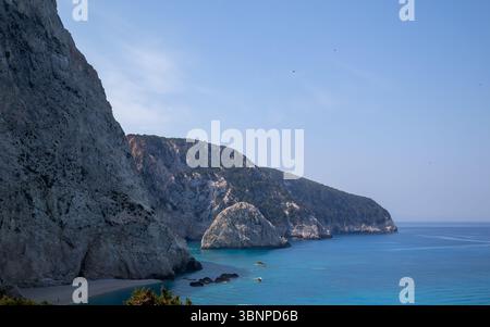 Atemberaubender Panoramablick auf einen abgeschiedenen griechischen Inselstrand mit hohen weißen Klippen, pulsierendem türkisfarbenem Meer und klarem blauem Himmel an einem sonnigen Sommertag. Stockfoto