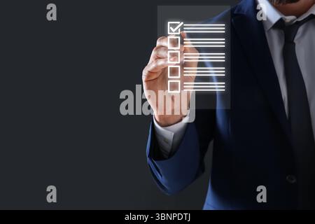 Geschäftsmann, der die Checkliste auf dem virtuellen Bildschirm vor dunkelgrauem Hintergrund ankreuzt, Nahaufnahme Stockfoto