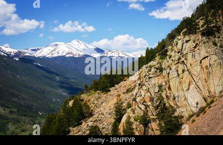 Ein zerklüfteter Granithang führt in kiefernbedeckte Hügel und schneebedeckte Gipfel nahe Silver Plume, Colorado. Klarer Himmel umrahmt diesen alpinen Blick. Stockfoto
