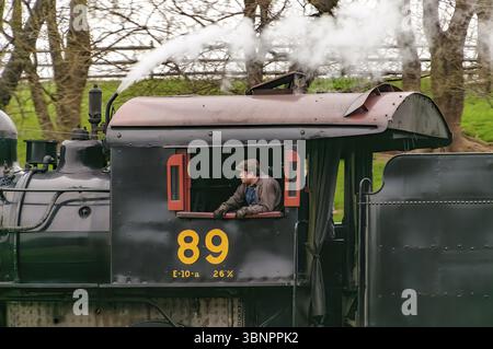 Strasburg, Pennsylvania, 7. April 2023 - Nahaufnahme eines Dampflokomotiven-Fahrerhauses mit den Feuerwehrleuten in der Eröffnung, während der Zug auf einer Wolke vorbeifährt Stockfoto