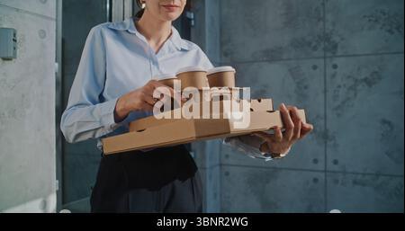 Liefermann übergibt Geschäftsfrau Zahlungsterminal nach erfolgreicher Pizzalieferung zum Bürogebäude. Frau hält Essen aus dem Restaurant, bezahlt für Bestellung kontaktlos mit Smartphone. Nahaufnahme. Stockfoto