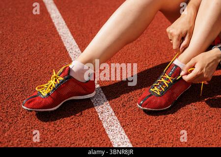 Nahaufnahme von Athleten, die Schnürsenkel auf der roten Laufbahn binden, die sich auf Outdoor-Workout Fitness und gesunden Lebensstil vorbereiten. Stockfoto