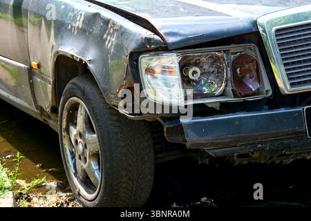 Altes Auto mit einem rostigen Flügel, einem kaputten Scheinwerfer und einem Platten Reifen Stockfoto