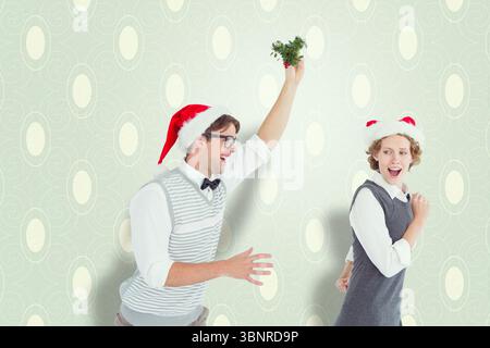 Verspielter kaukasier mit weihnachtsmütze und einem kleinen weihnachtsbaum, der hinter der Freundin läuft Stockfoto