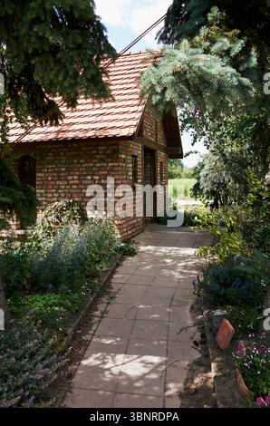 Backsteinhaus mit einem roten Dach und einem Weg, der dorthin führt. Das Haus ist von einem Garten mit vielen Pflanzen und Blumen umgeben. Warschau, Polen 30-6-2025 Stockfoto