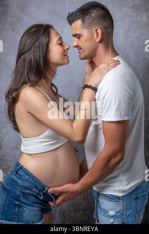 Ein Mann ist dabei, seine schwangere Partnerin zu küssen, während er ihren Bauch mit den Händen hält Stockfoto