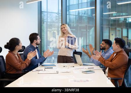 Ein vielseitiges Team applaudiert seinem Kollegen in einer Büroumgebung und feiert Erfolg und Teamarbeit. Stockfoto
