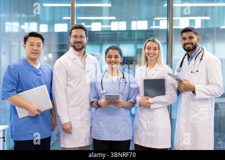 Ein vielfältiges Team von Medizinern, darunter Ärzte und Krankenschwestern, lächelt in einer modernen Gesundheitseinrichtung in die Kamera. Stockfoto