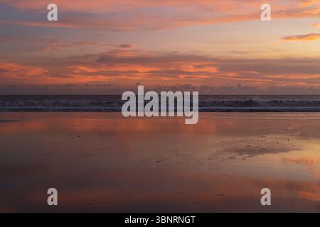 Lebendiger Sonnenuntergang am tropischen Strand, der sich bei Ebbe auf nassem Sand spiegelt Stockfoto