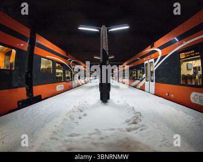 Moderne orangene Personenzüge am verschneiten Bahnsteig in der Nacht, Estland. Stadler Zug Stockfoto