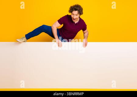 Energiegeladener junger Mann mit lockigem Haar, der auf einem leuchtend gelben Hintergrund posiert und stilvolle Freizeitmode und dynamischen Ausdruck zeigt. Stockfoto