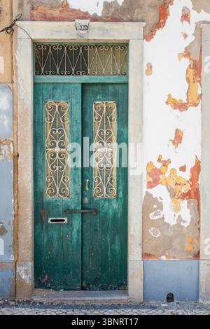 Alte grüne Holztür mit schmiedeeisernen Details und abblätternder Farbe, Algarve, Portugal. Stockfoto