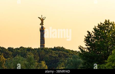 Die Siegessäule Berlins erhebt sich bei einem goldenen Sommeruntergang über den Bäumen des Tiergartens, der sich am Abendhimmel abhebt. Stockfoto