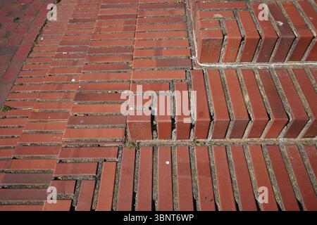 Eine Nahansicht eines Gehwegs im Freien und einer Treppe aus rotem Backstein. Die Steine sind in verschiedenen geometrischen Mustern angeordnet, wodurch ein reicher Bogen entsteht Stockfoto