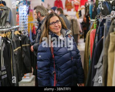 Vereinigtes Königreich, London, 07. Juli 2025. Frau mit blauer Winterjacke, die in einem Second-Hand-Geschäft in London, Surround, in Vintage-Kleiderständer stöbert Stockfoto