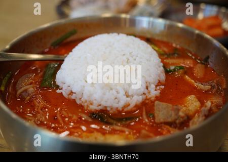 Nahaufnahme der koreanischen scharfen Schweinesuppe mit einer ganzen Schüssel mit gedämpftem weißem Reis, die in einer Messingschüssel auf die Oberseite geklappt wird Stockfoto
