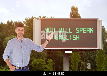 Lehrer, der auf Text zeigt, spricht Englisch auf digitalen Plakaten im Freien. Sprachkurs Stockfoto