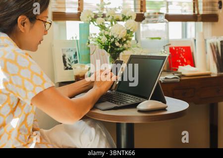 Geschäftsfrau benutzt Handy, während sie am Laptop arbeitet. Stockfoto
