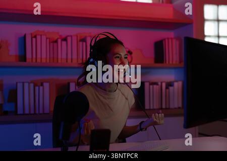 Fröhlicher Gamer in Aktion. Junge Frau feiert einen Sieg, während sie mit einem Headset in einem stilvollen Raum spielt. Stockfoto