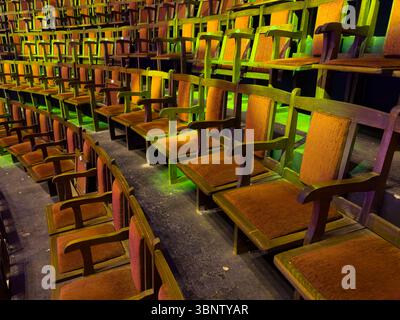 Reihen leerer Vintage-Holzsitze in einem geschwungenen Auditorium mit farbiger Bühnenbeleuchtung. Keine Personen. Nützlich für redaktionelle oder gestalterische Hintergründe. Stockfoto