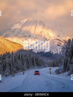 SUV fahren bei Sonnenaufgang auf einer verschneiten Panoramastraße in den Kananaskis Country, Alberta, Kanada Stockfoto