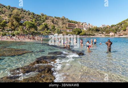 Taormina, Sizilien, Italien - 29. September 2024: Menschen spazieren durch das Wasser zwischen dem Strand und der Isola Bella in Taormina. Stockfoto