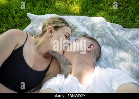 Ein romantisches Paar genießt einen liebevollen Kuss, während es auf einer Decke in einem grünen Park sitzt Stockfoto