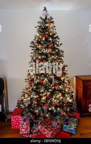 Geschmückter weihnachtsbaum mit eingewickelten Geschenken darunter an einer weißen Wand Stockfoto