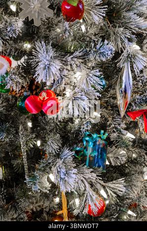 Nahaufnahme von Dekorationen an einem Weihnachtsbaum mit roten Ornamenten unter den Kiefernnadeln. Stockfoto