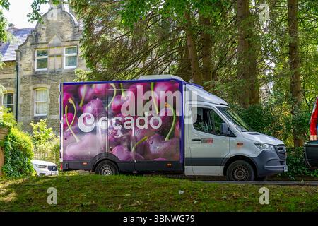 Buxton, Derbyshire, Großbritannien, 28. Juni 2025: Ocado Food Delivery Truck mit lebendigem Kirschdesign in einer üppigen, grünen Wohngegend. Stockfoto