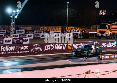Motion Blur Drag Racing bei Nacht, bei dem Autos auf der Rennstrecke mit Zuschauern in der Nähe konkurrieren Stockfoto