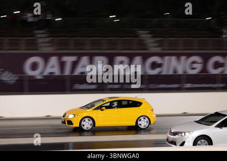 Motion Blur Drag Racing bei Nacht, bei dem Autos auf der Rennstrecke mit Zuschauern in der Nähe konkurrieren Stockfoto