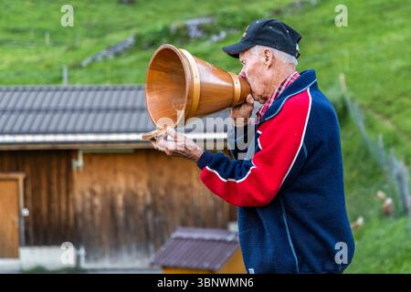 Sepp Zurfluh übernahm 1970 die Hobiel Alp von seinem Vater. Er hat bereits 69 Sommer hier verbracht. Am Abend ruft er den Alpsegen, auch Betruf genannt, in allen vier Richtungen zum umfassenden Schutz vor Gefahren auf. Er verwendet einen hölzernen Milchtrichter (Folle), um seine Stimme zu verstärken. Abendritual in der alpinen Landschaft auf der Hobiel-Alp bei Engelberg, Schweiz. Das älteste Familienmitglied führt den traditionellen Gebetsruf vor allen Anwesenden aus. Diese Tradition zeigt die Kombination von tiefer Frömmigkeit und der beeindruckenden Natur der Schweizer Alpen. Hobiel, Engelberg, Uri Stockfoto