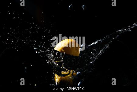 Zitronenhälfte und Heidelbeeren in dramatischem Spritzen, gefangen in der Luft mit schwebenden Wassertröpfchen. Leuchtende Früchte in Hochgeschwindigkeitsaufnahmen von Makrokost. Stockfoto