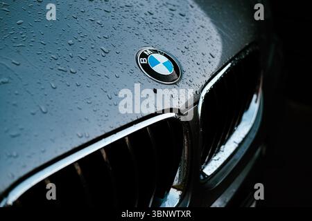 Nahaufnahme einer BMW Motorhaube mit Regentropfen auf dem Logo und einer glänzenden Oberfläche. Die Motorhaube eines SUV-Autos mit dem Emblem, das von Regentropfen bedeckt ist. sle Stockfoto