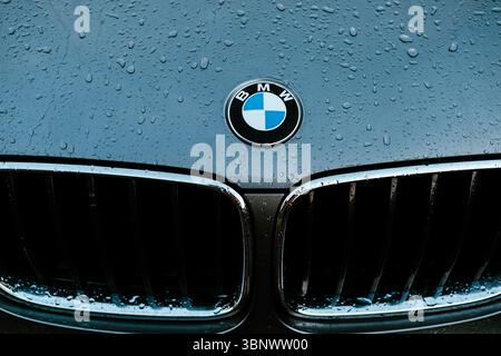 Nahaufnahme einer BMW Motorhaube mit Regentropfen auf dem Logo und einer glänzenden Oberfläche. Die Motorhaube eines SUV-Autos mit dem Emblem, das von Regentropfen bedeckt ist. sle Stockfoto